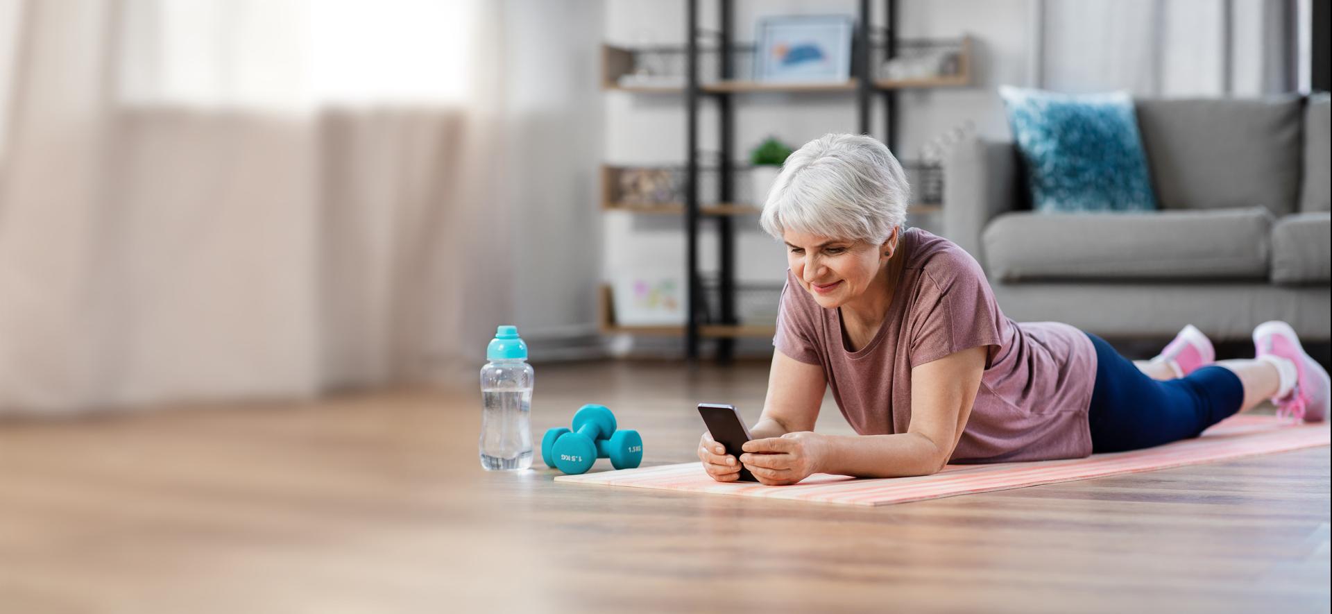 starsza kobieta leżące na macie do ćwiczeń z telefonem w ręku