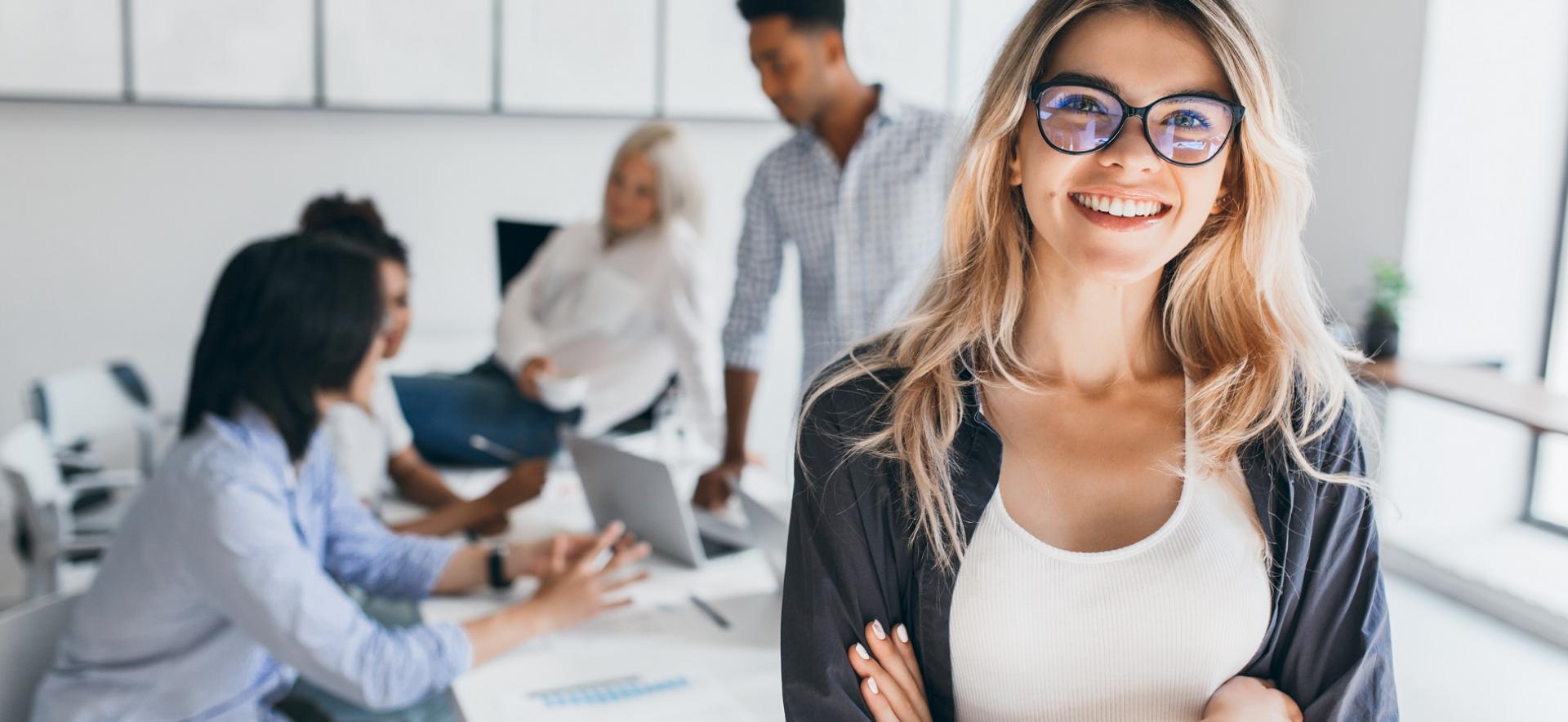 Młoda kobieta, w tle kobiety i mężczyzni siedzących przy stole