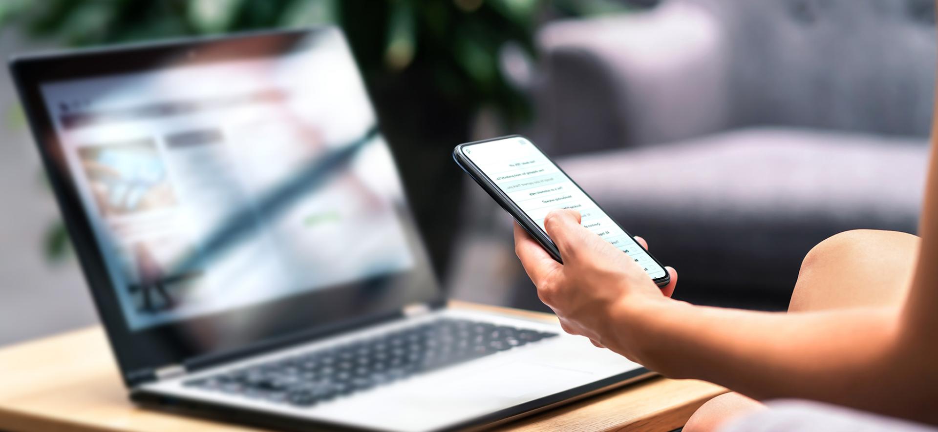 Laptop, ręka osoby trzymającej smartfona