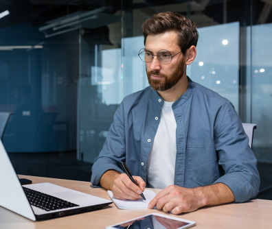 mężczyzna przy komputerze robiący notatki 