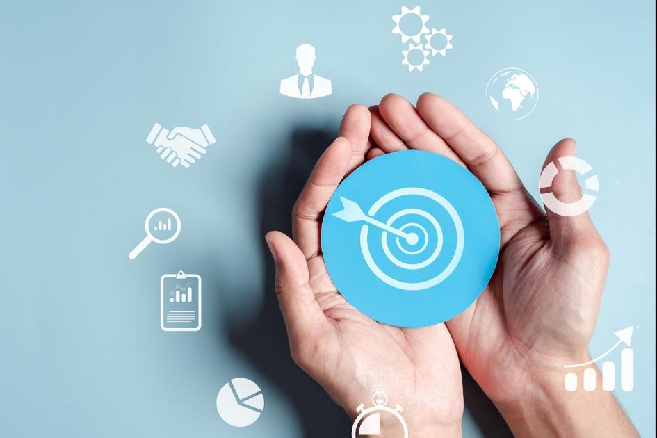 dłonie trzymające grafikę ze znaczkiem strzału w dziesiątkę, wokół infografiki
