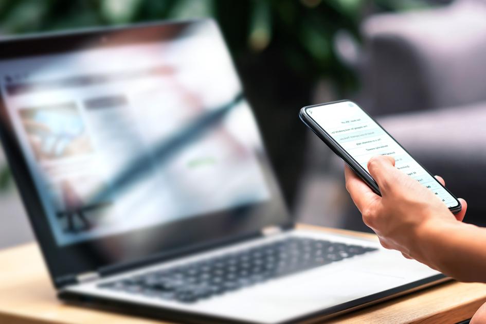 Laptop, ręka osoby trzymającej smartfona 